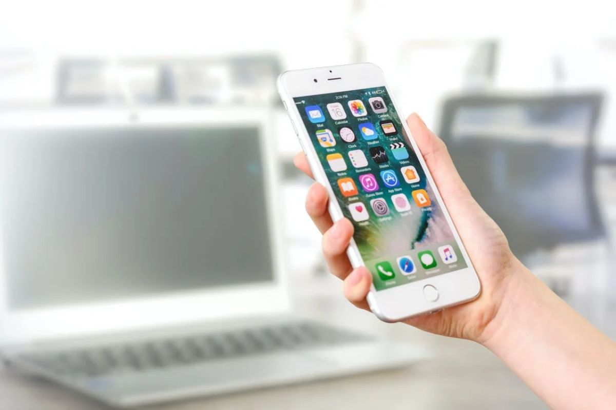 iPhone: Aplicativos gratuitos Aplicativos gratuitos em tela de iPhone com notebook e monitores ao fundo em desfoco