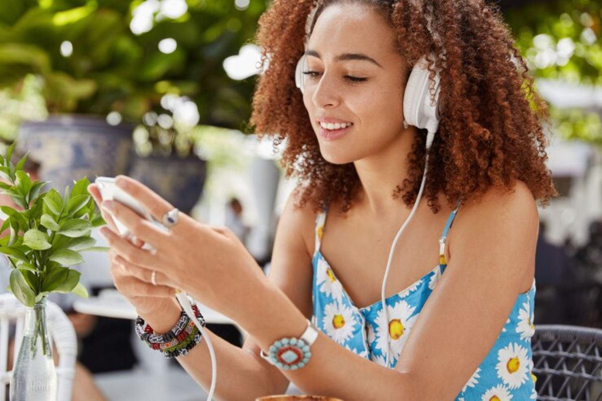 Mulher usando celular com fone de ouvido tipo headset e aproveitando Aplicativos para baixar música