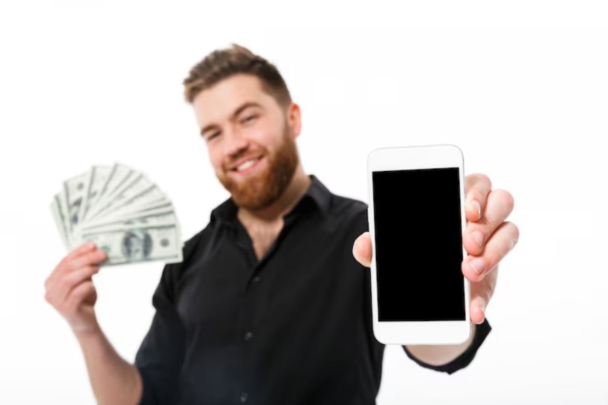 Notas: Aplicativos para ganhar dinheiro Homem com notas de dólar na mão e celular na outra usando Aplicativos para ganhar dinheiro
