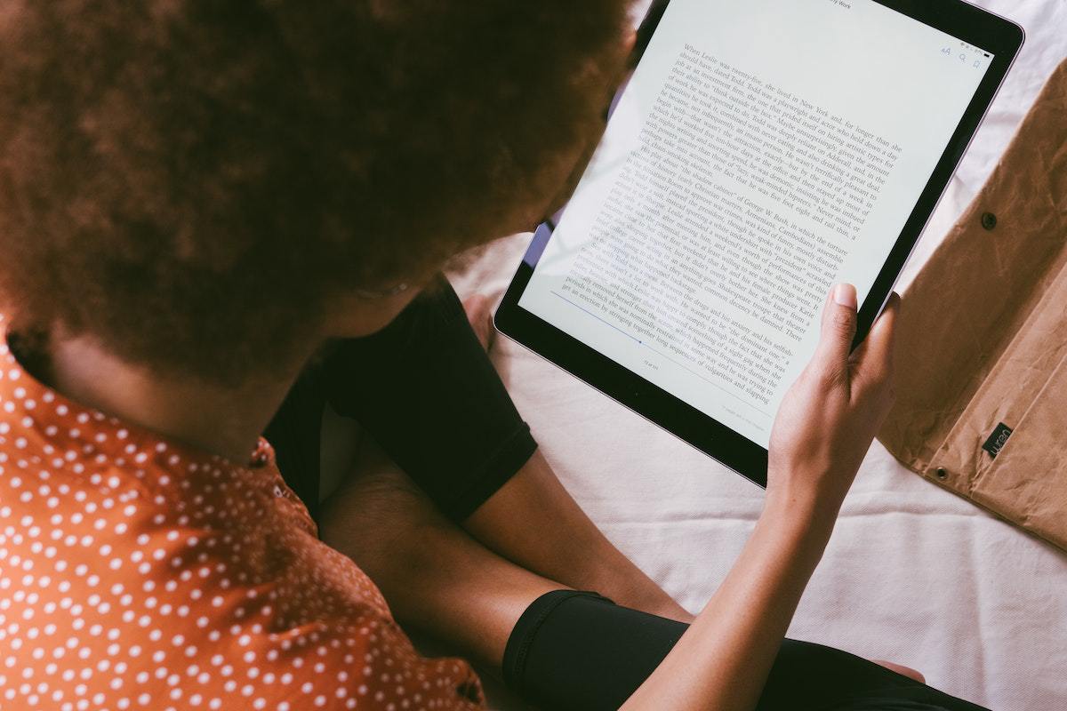Conteúdo: Apps de livros grátis Mulher lendo conteúdo em um dos Apps de livros grátis sentada em local análogo à cama