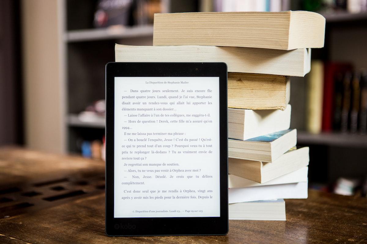 Apps de livros grátis em tablet preto apoiado sobre livros físicos sobre mesa de madeira