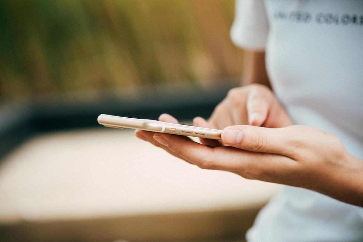 Mulher com celular na mão em ambiente em desfoco ao fundo de fotografia