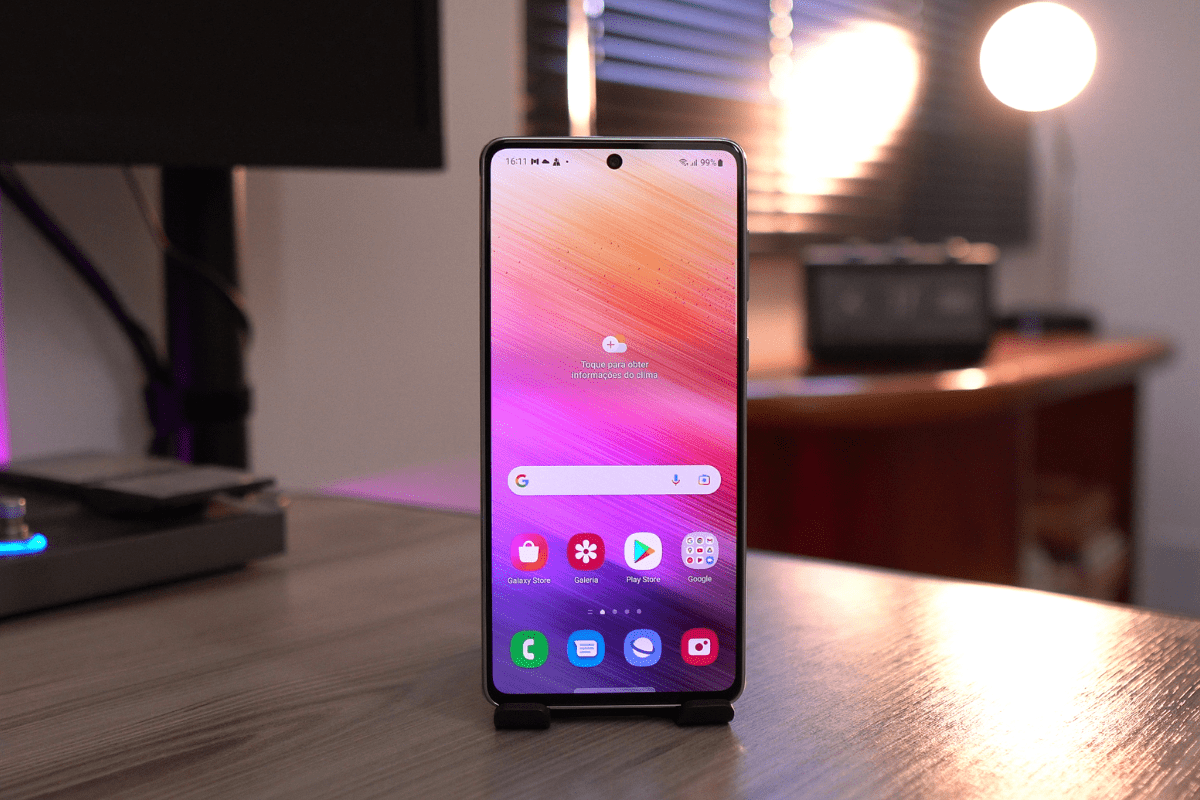 Tela: Galaxy A73 Galaxy A73 em suporte de pé com tela virada para foto sobre mesa de madeira em interior de casa