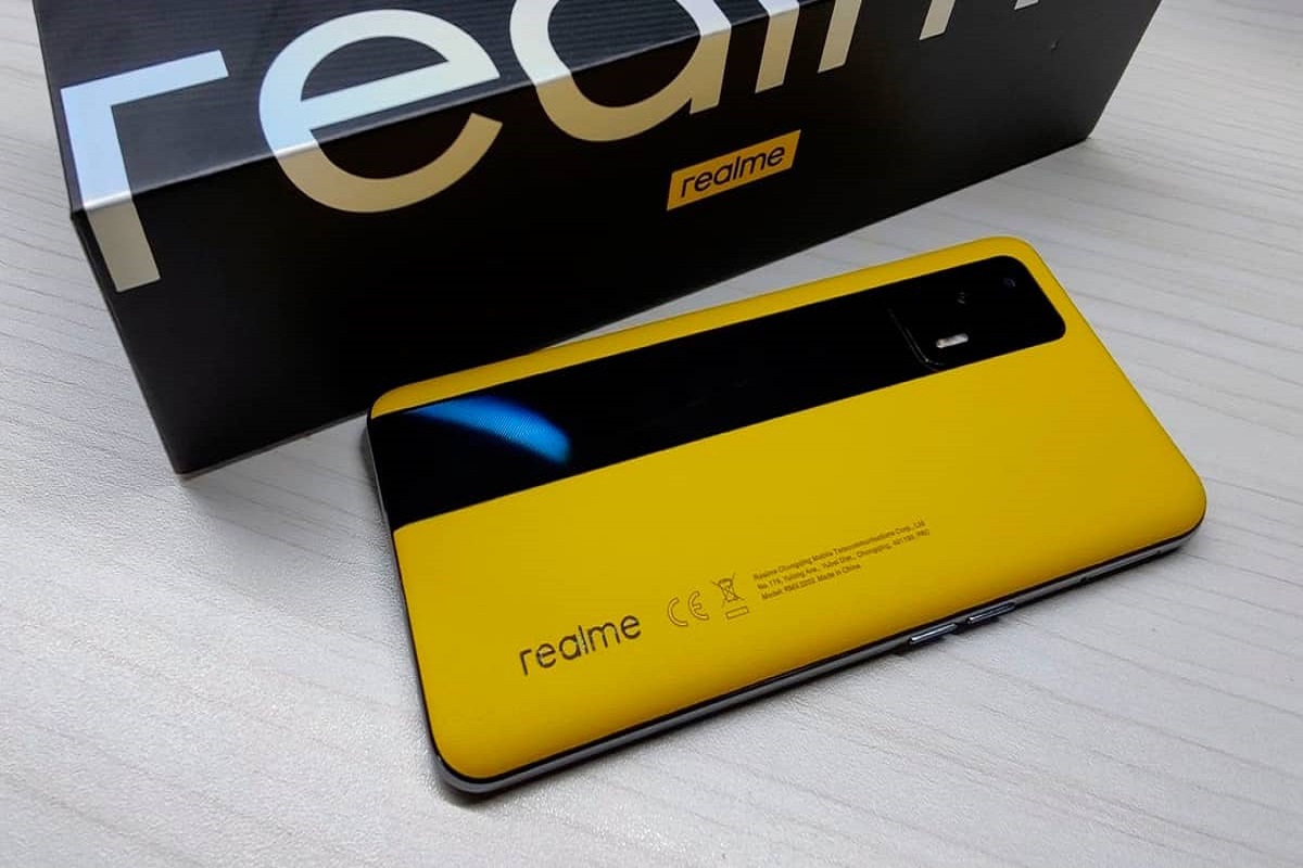 Realme GT com tela virada para baixo em mesa de madeira ao lado de sua caixa