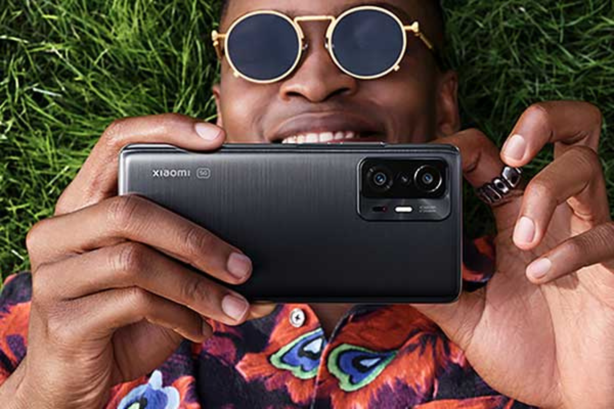 Usuário: Xiaomi 11T Usuário com seu Xiaomi 11T deitado no chão sobre grama sorridente enquanto mexe no produto como se ampliasse algo na tela do celular