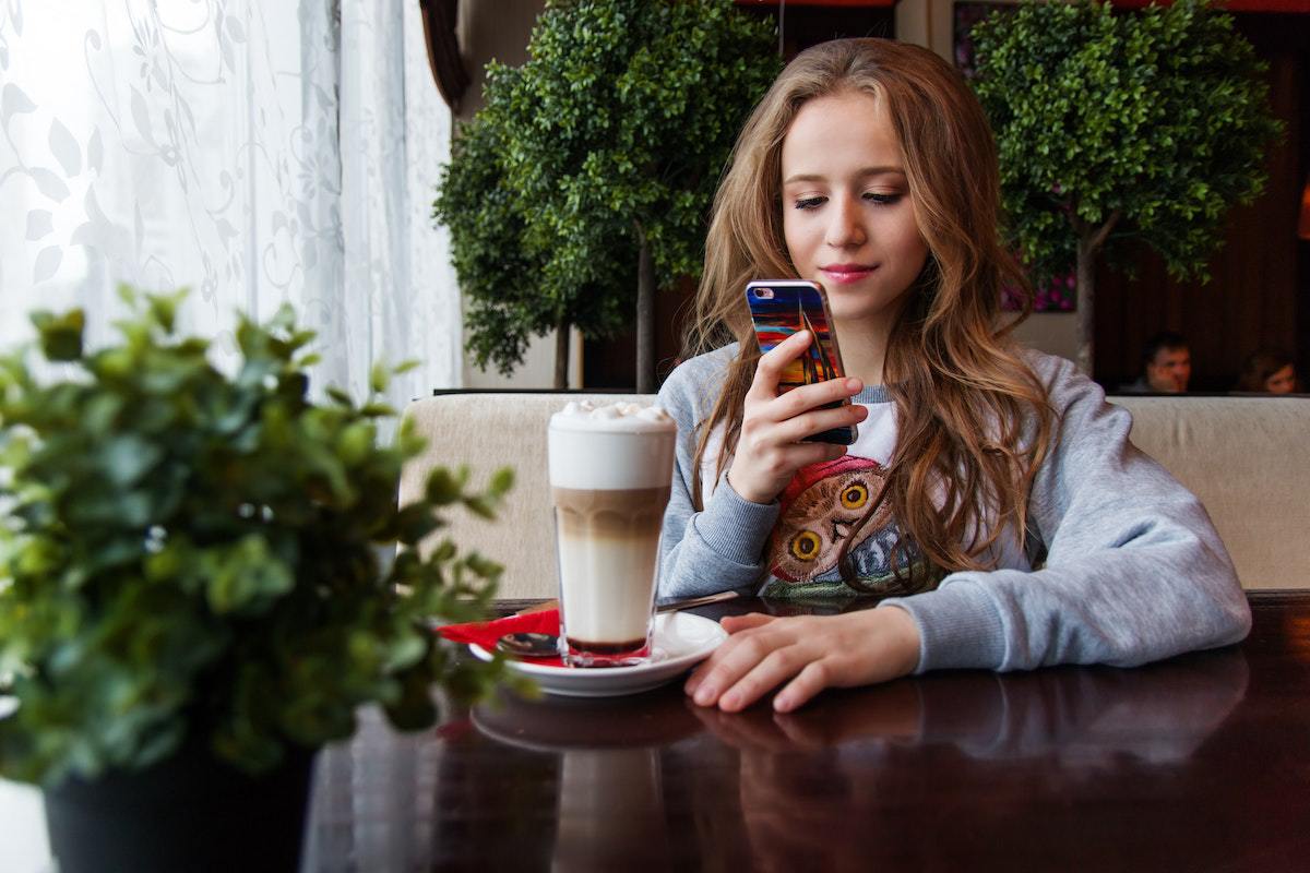 Mulher usando Apps para aprender inglês no smartphone em restaurante e com copo de bebida à sua frente
