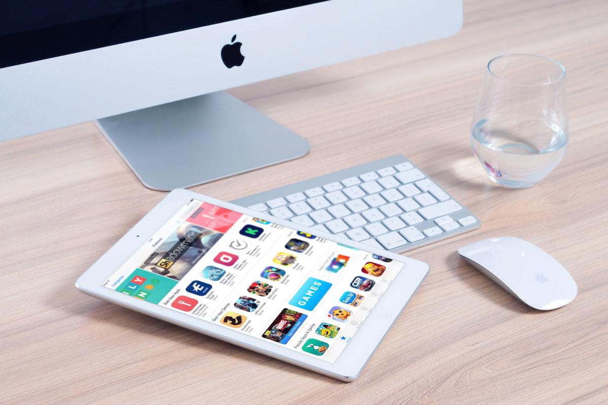 Tablet branco sobre mesa de madeira com loja de aplicativos buscando Apps para aprender inglês