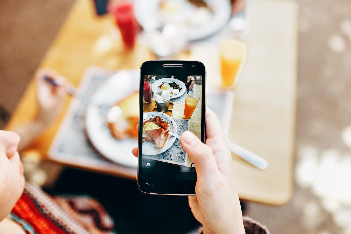 Mulher em restaurante com Celular barato tirando foto de prato