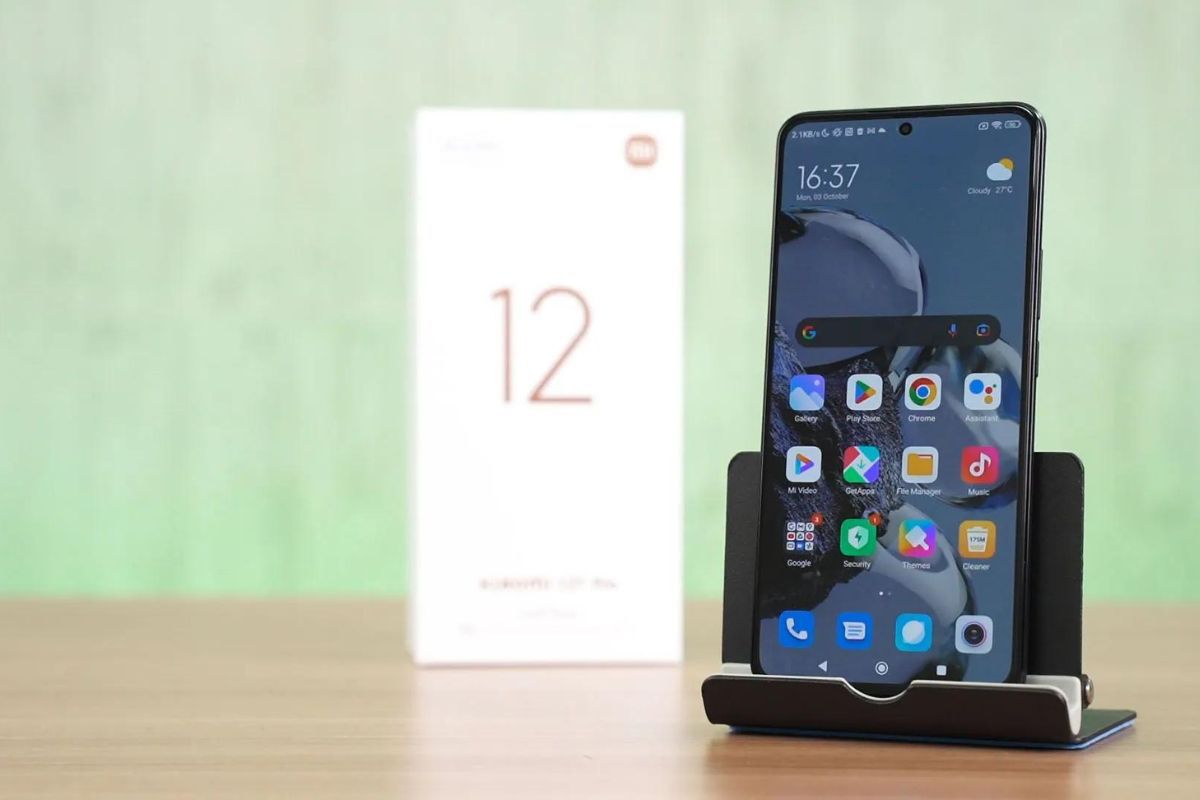 Xiaomi 12T Pro preto apoiado em suporte sobre mesa de madeira ao lado da sua caixa, de pé com tela desbloqueada mostrando tela inicial com apps